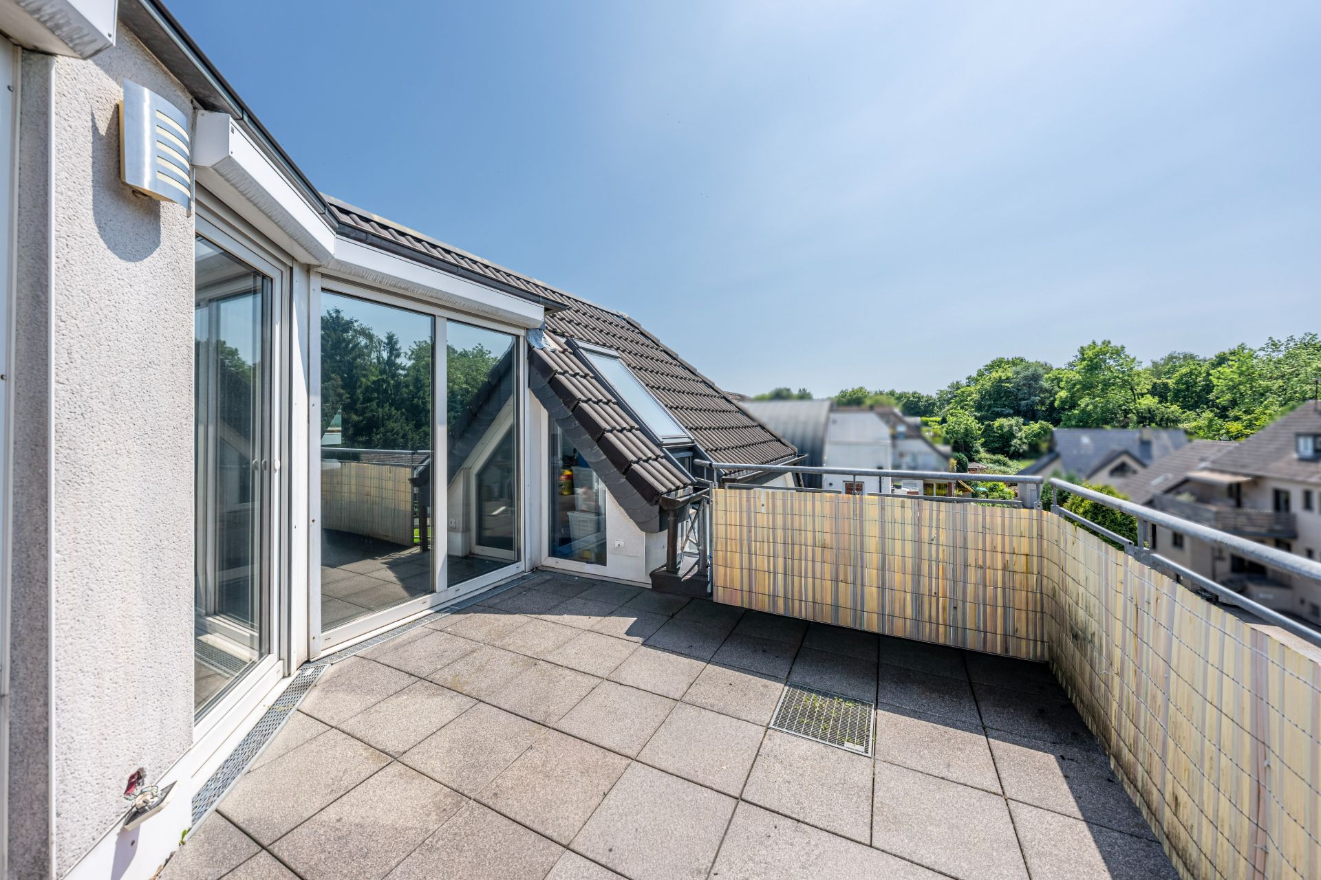 Große Dachterrasse mit Fliesenboden und Glas-Schiebetüren, Ausblick auf Bäume und Nachbarhäuser.
