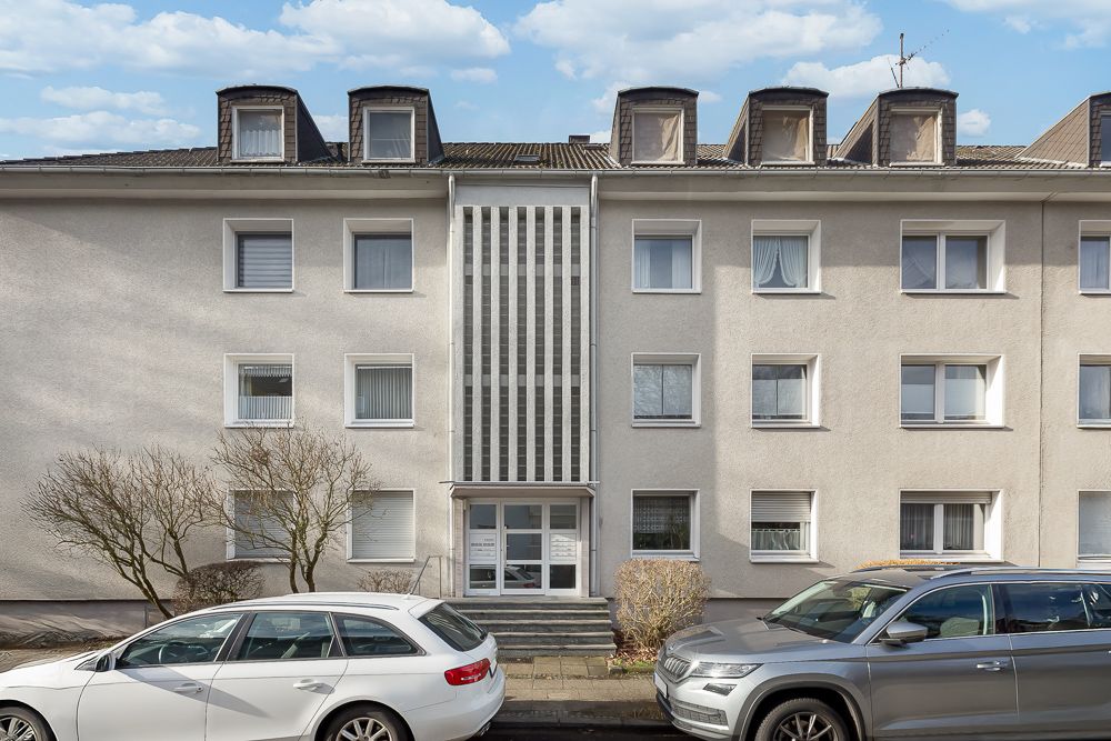 Dreistöckiges Wohnhaus mit mehreren Fenstern und parkenden Autos davor.