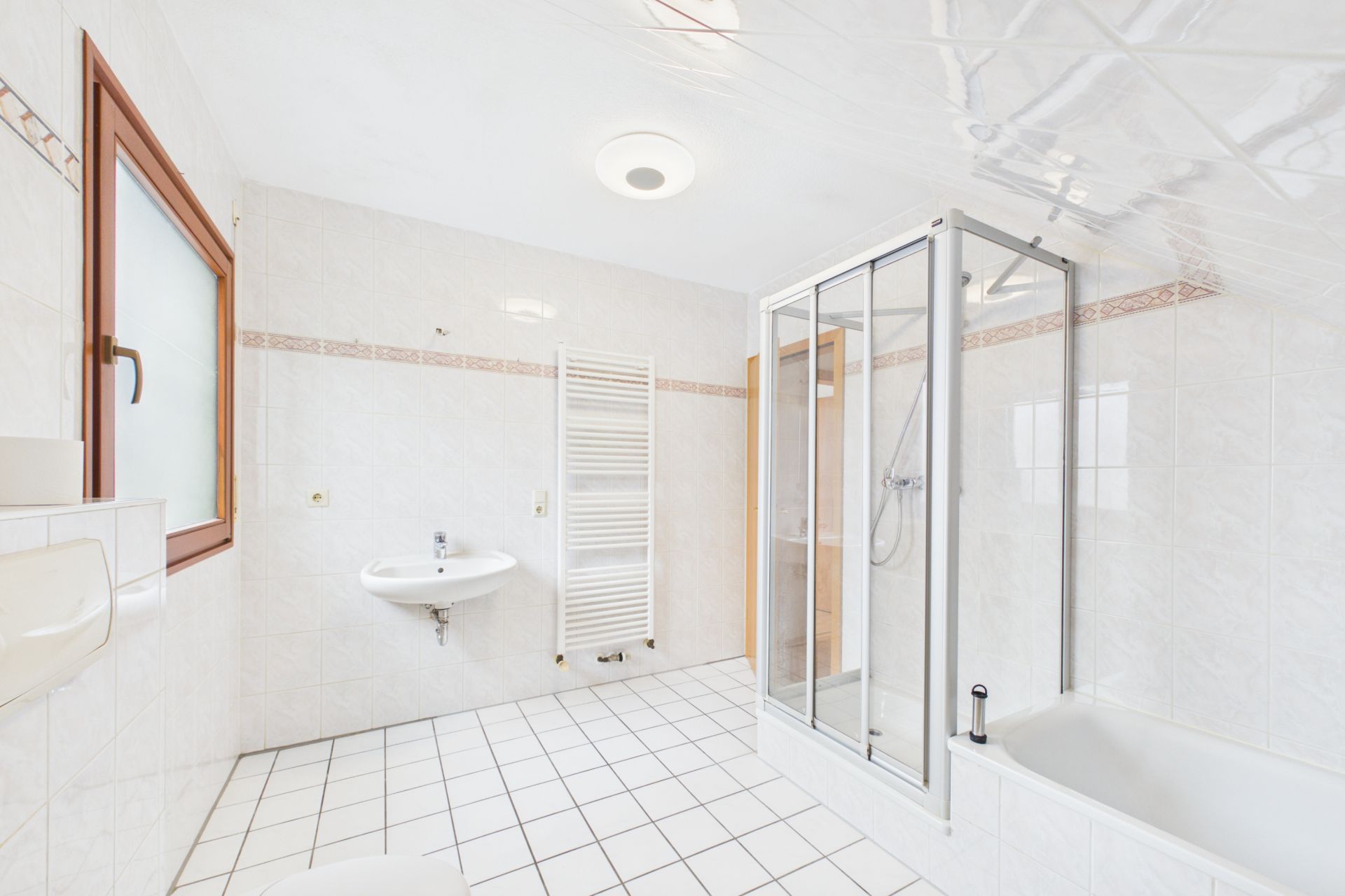 Helles Badezimmer mit Fenster, Duschkabine, Badewanne, Waschbecken und Handtuchheizkörper.