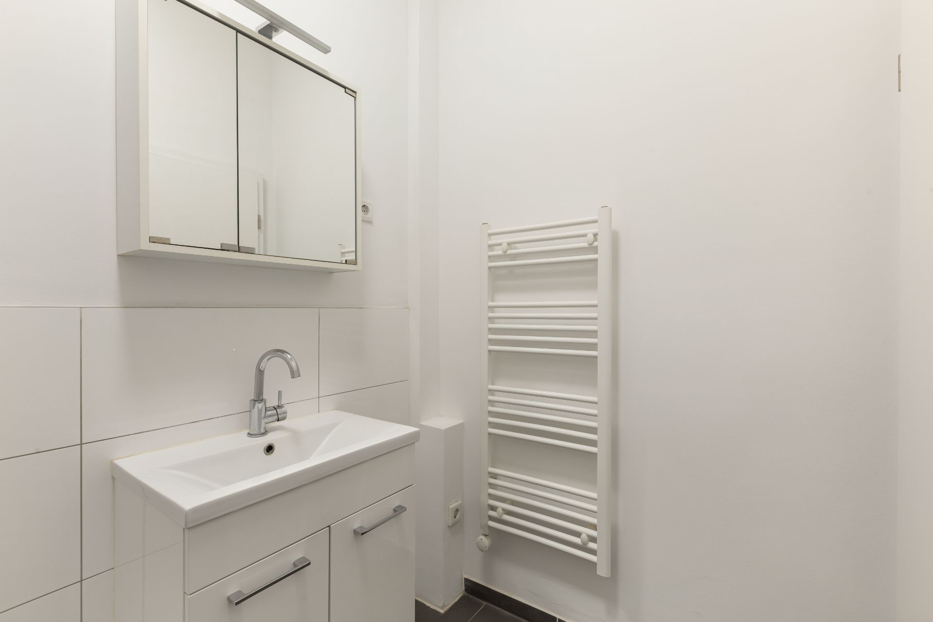 Modernes Badezimmer mit Waschbecken, Spiegelschrank und Handtuchheizkörper.