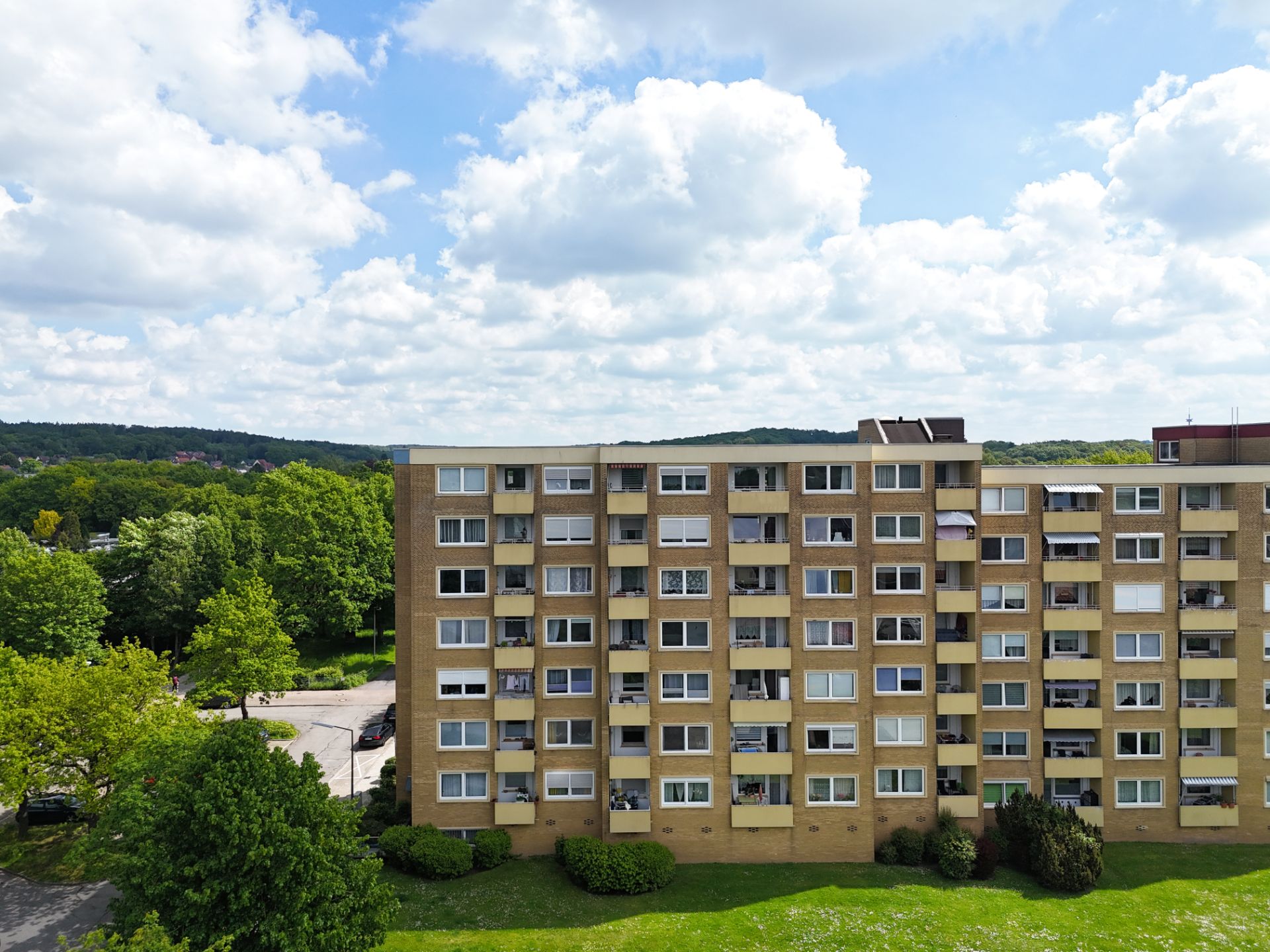 Mehrstöckiges Wohnhaus mit Balkonen und grüner Wiese davor, Bäume im Hintergrund.