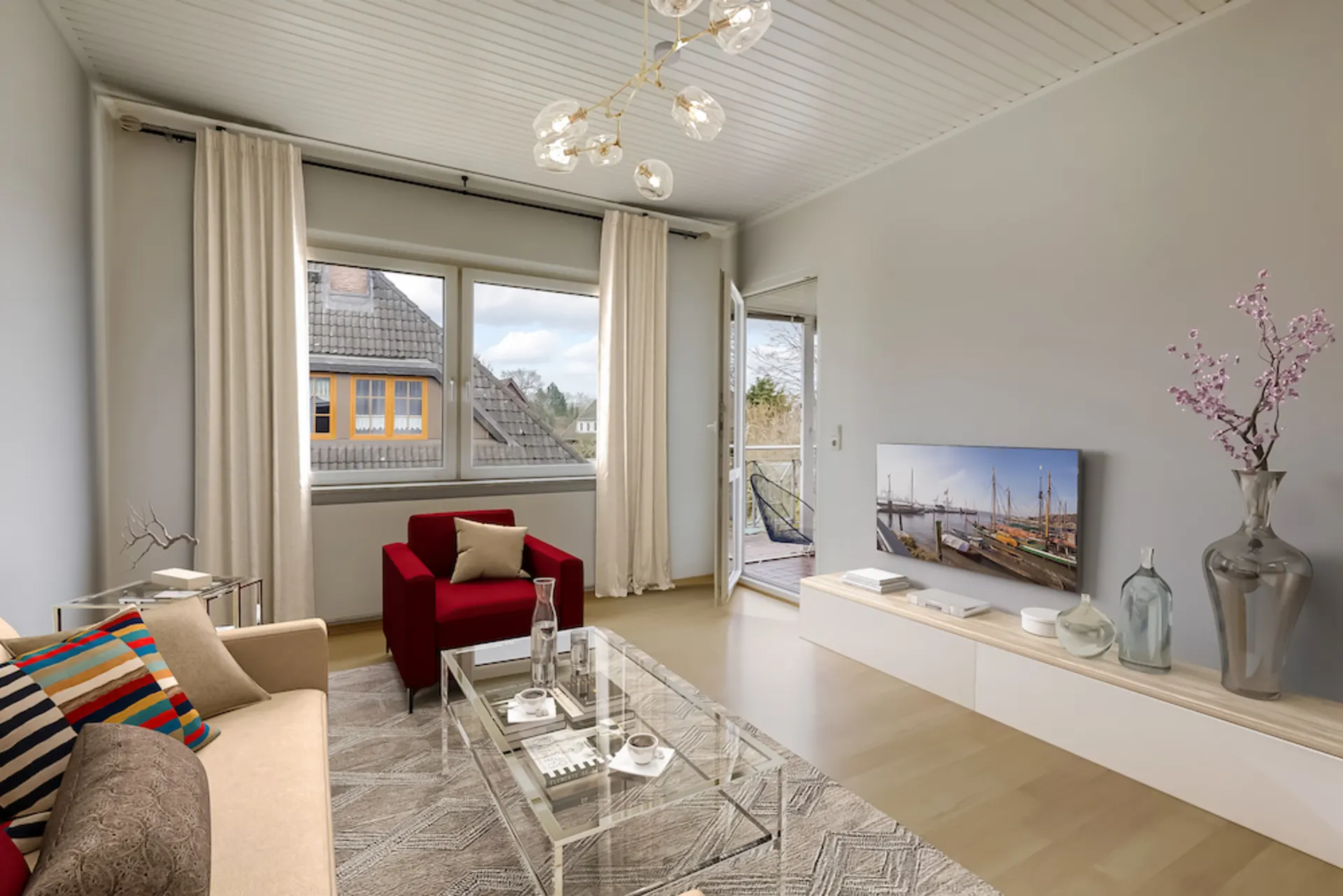 Modernes Wohnzimmer mit Sofa, rotem Sessel, TV, Glastisch und Zugang zum Balkon.