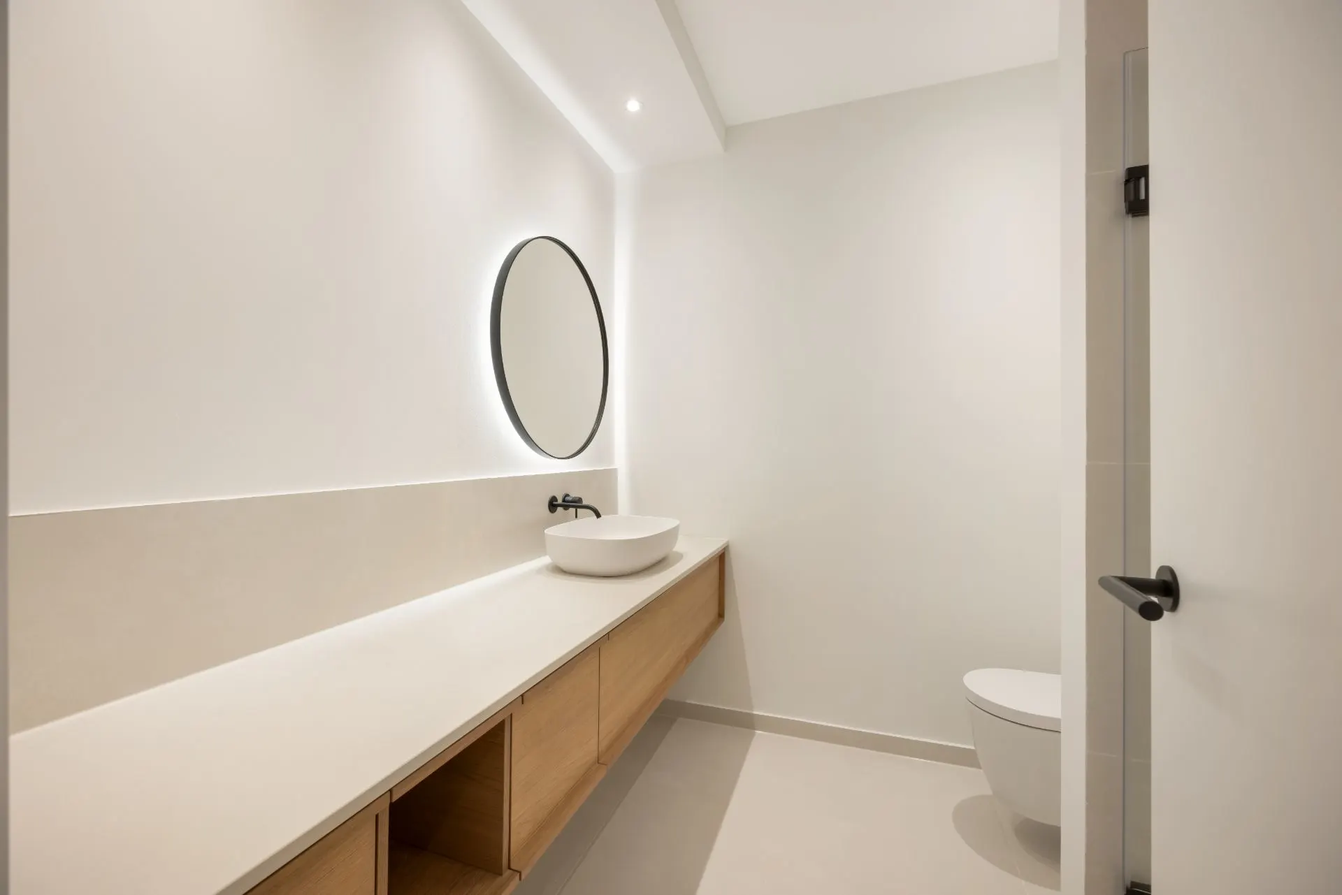 Modernes, helles Badezimmer mit rundem Spiegel, Waschbecken und Holzmöbeln.