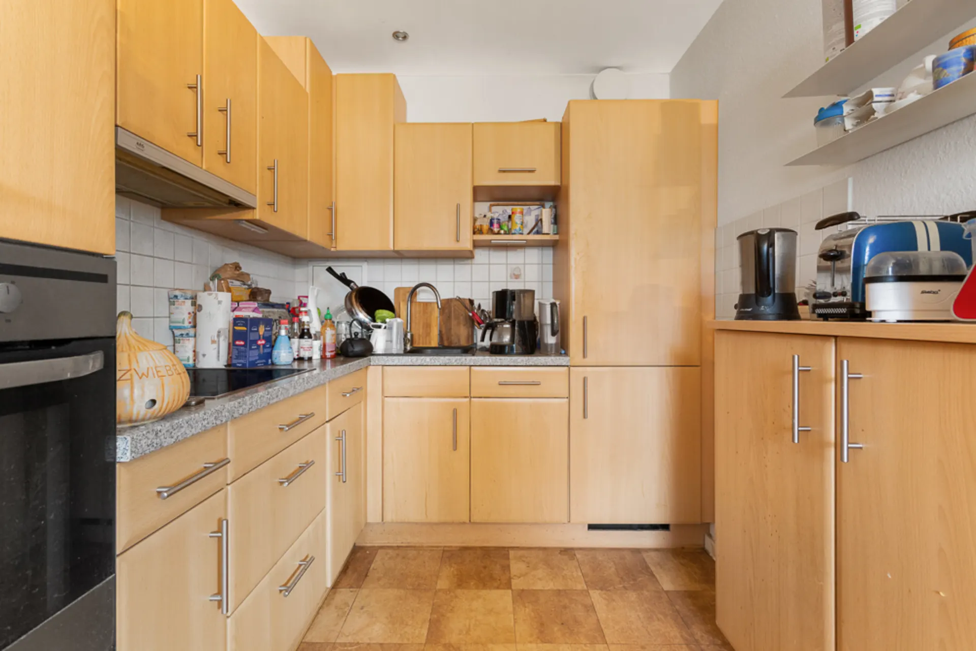 Küche mit Holzschränken, Arbeitsplatte, Küchengeräten und Regalen mit Geschirr.