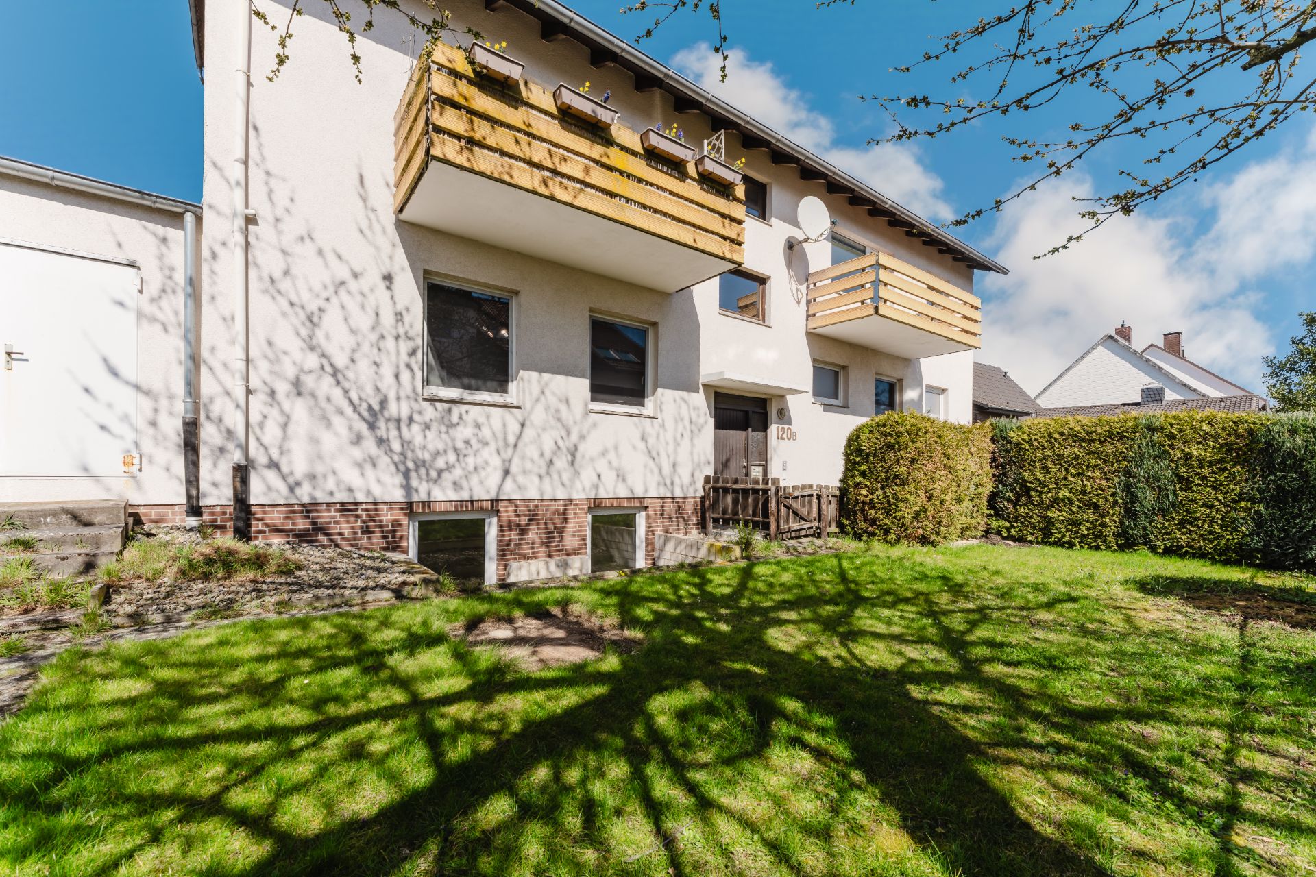 Zweistöckiges Wohnhaus mit Holzbalkonen und gepflegtem Garten im Vordergrund.