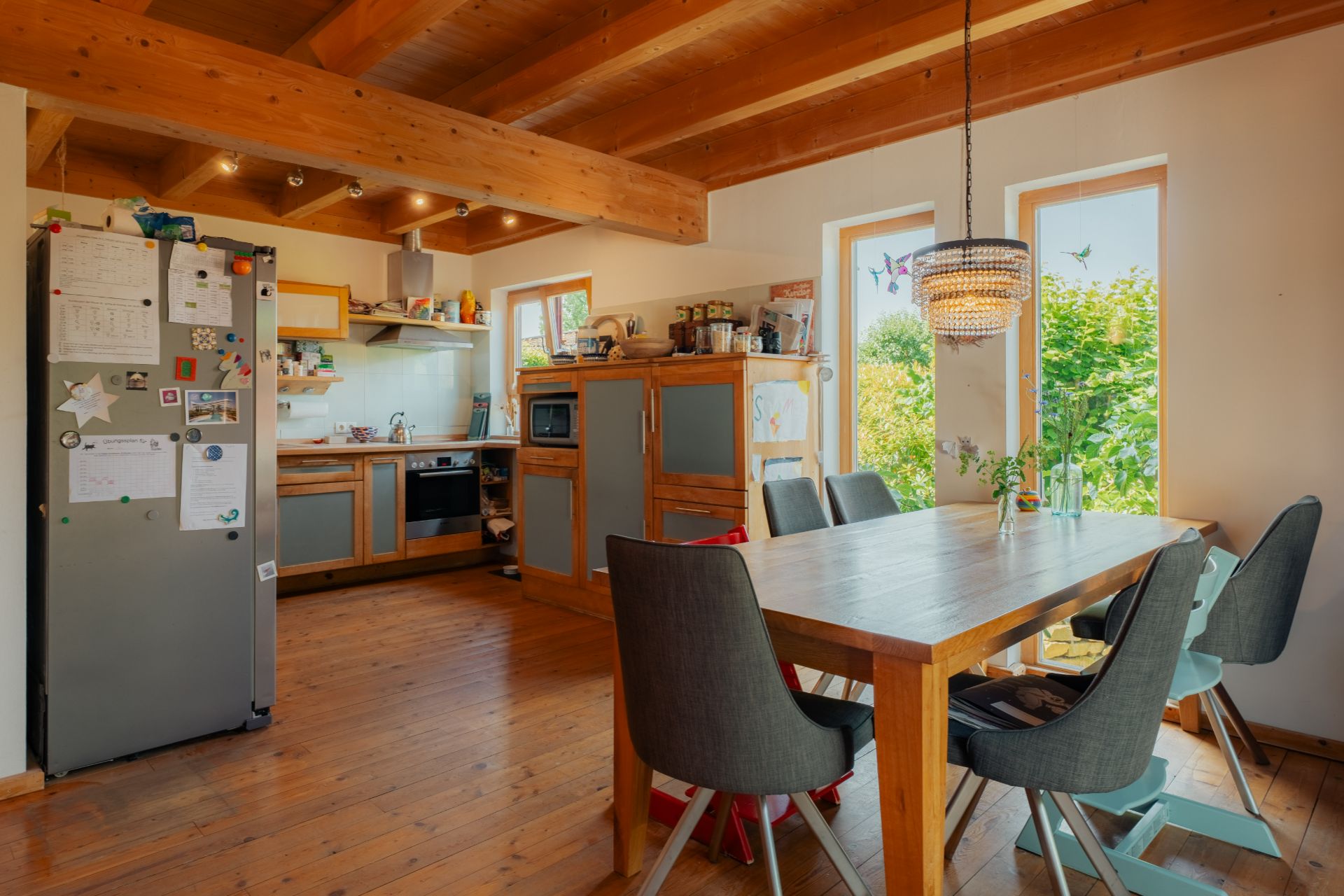 Holzküche mit Esstisch, sechs Stühlen, Kühlschrank und Fenstern, die nach draußen zeigen.