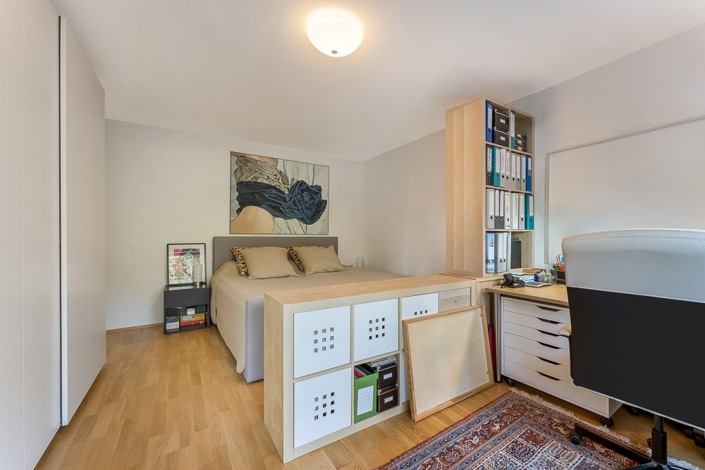 Helles Schlafzimmer mit Doppelbett, Schreibtisch, Regalen und Teppich auf Holzfußboden.