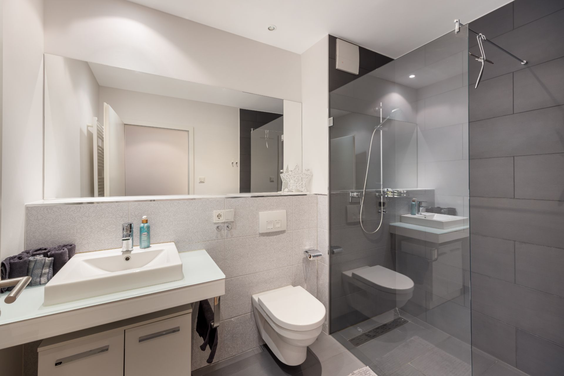 Modernes Badezimmer mit Waschbecken, Spiegel, Toilette und offener Dusche mit Glaswand.