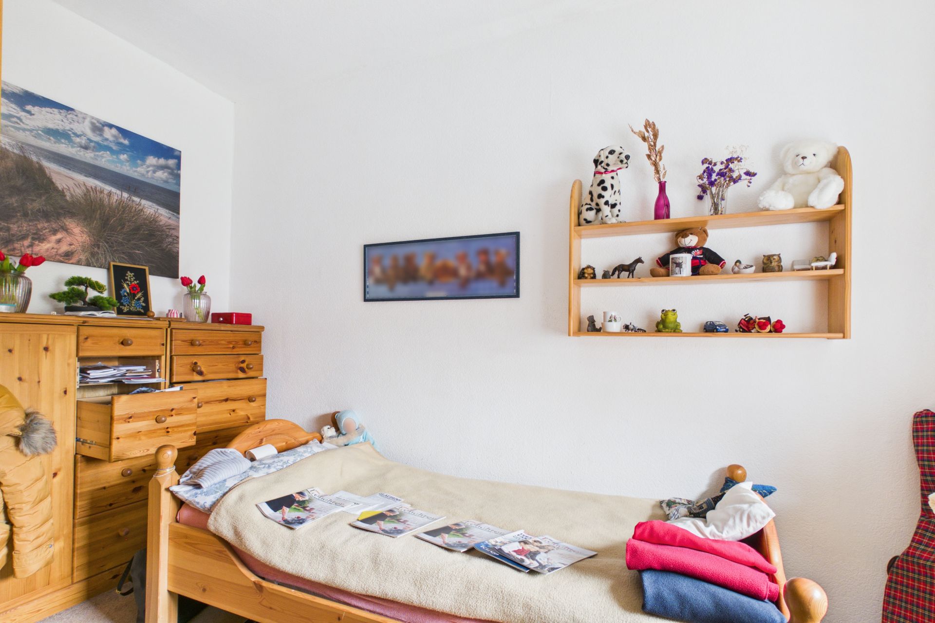 Kleines Schlafzimmer mit Holzbett, Kommode, Wandregal und Dekorationen.