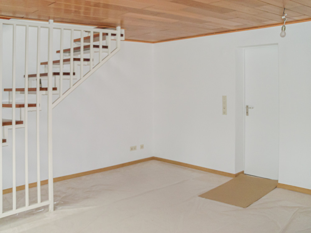 Leerer Raum mit weißer Wand, Treppe, Holzboden und einer geschlossenen weißen Tür.