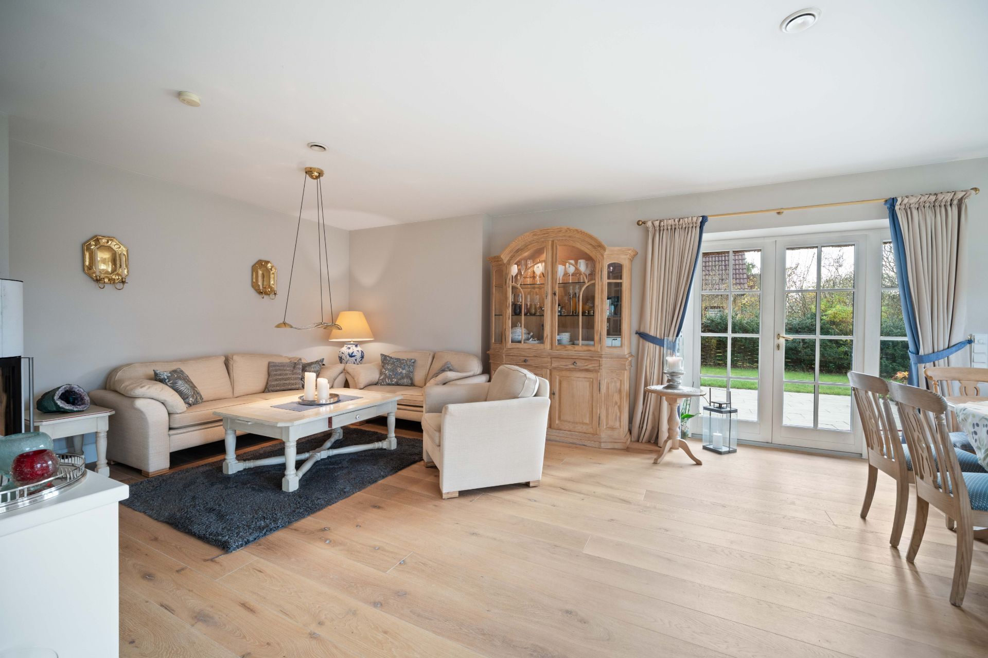 Helles Wohnzimmer mit Sofa, Sessel, Holzboden und Glastüren zum Garten.