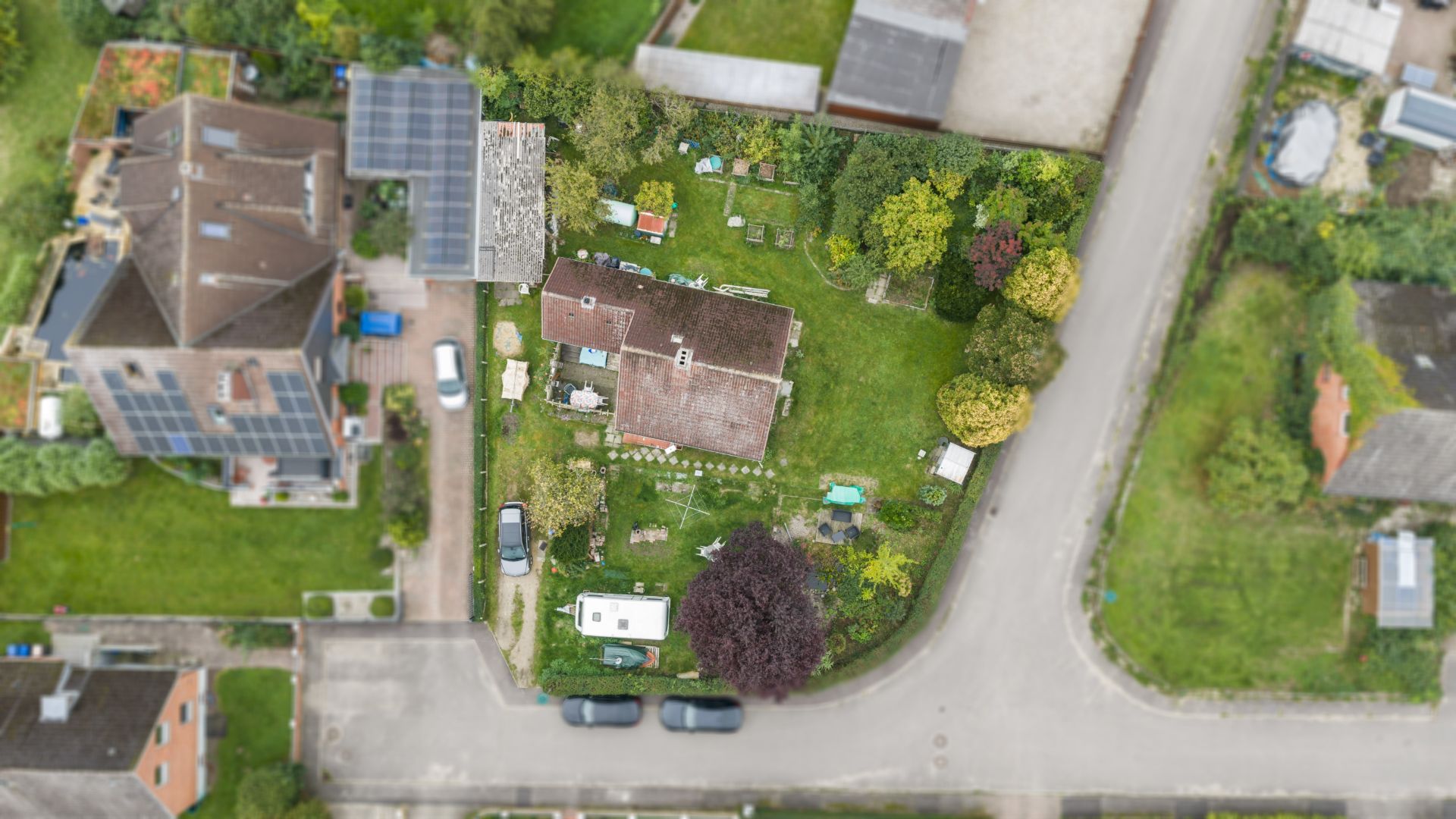 Luftaufnahme eines Hauses mit großem Garten an einer Straßenecke.