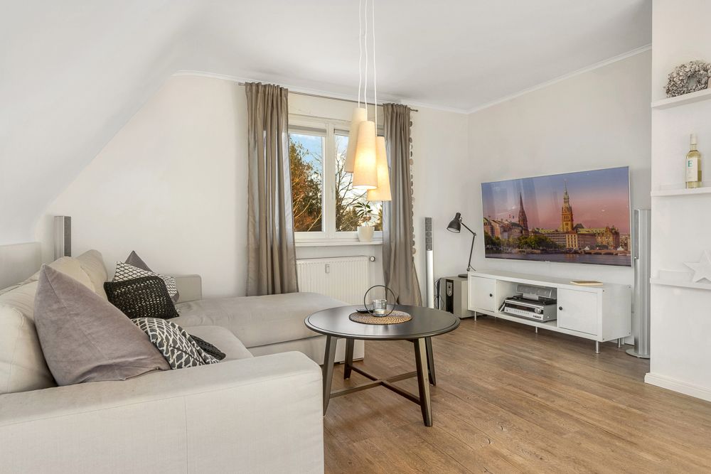 Wohnzimmer mit Ecksofa, Couchtisch, Stehlampe, Fernseher und großem Fenster.