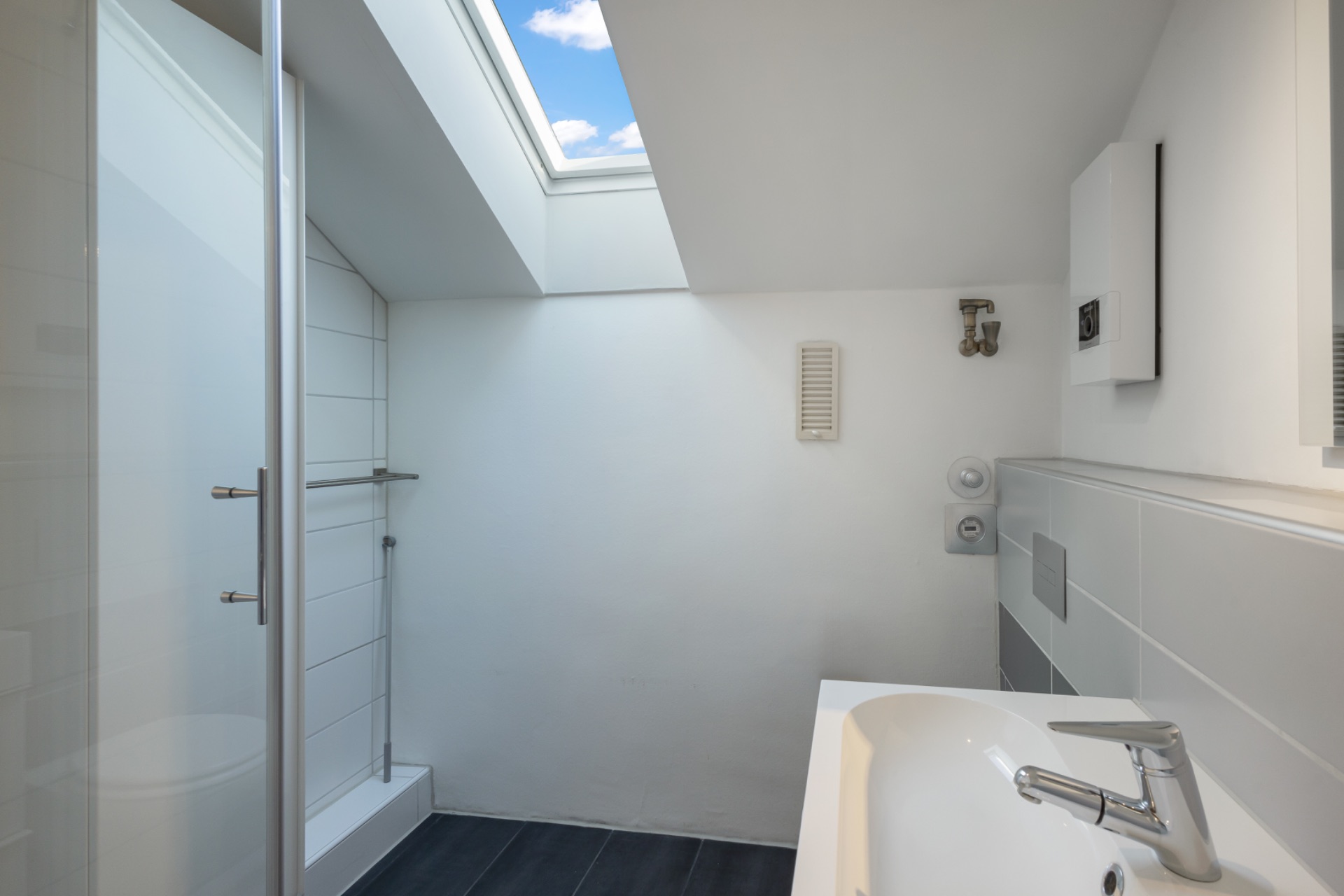 Modernes Badezimmer mit Dachfenster, Dusche und weißem Waschbecken.