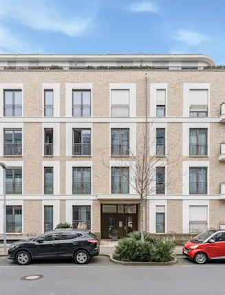 Modernes Wohngebäude mit Balkonen, großen Fenstern und parkenden Autos davor.