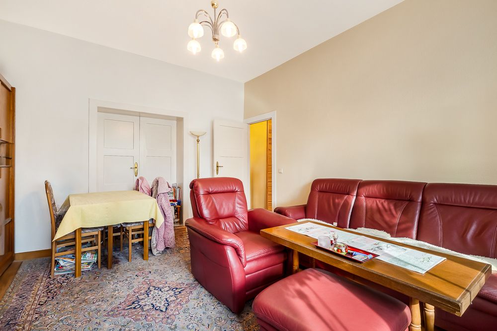 Wohnzimmer mit roten Ledersofas, Holztisch und Esstisch mit gelber Tischdecke.