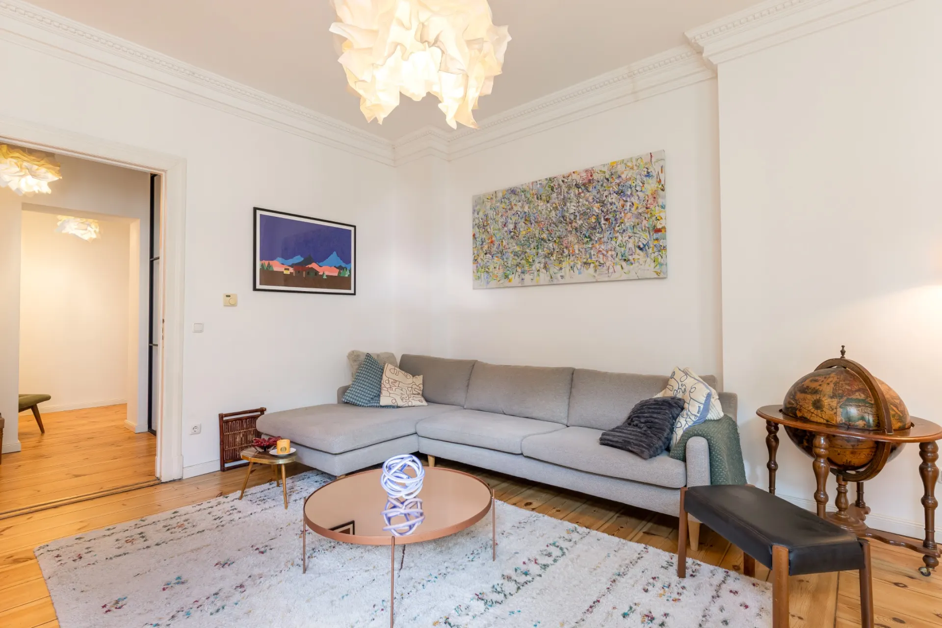 Helles Wohnzimmer mit grauem Ecksofa, Couchtisch, Teppich und Wandbildern.
