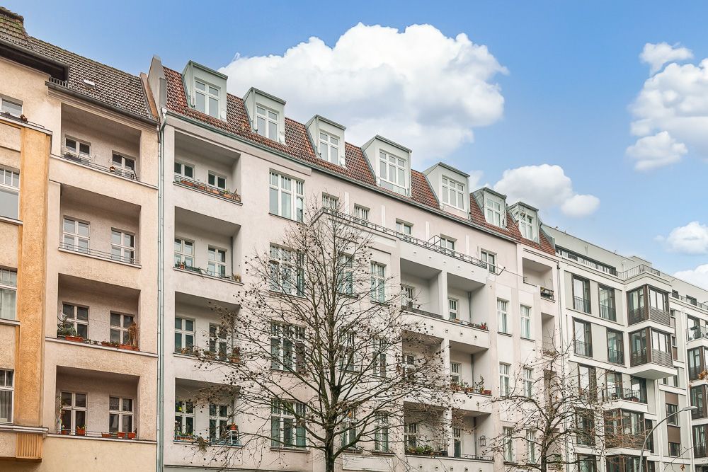 Mehrstöckiges Wohngebäude mit Balkonen und Fenstern, davor stehen Bäume.