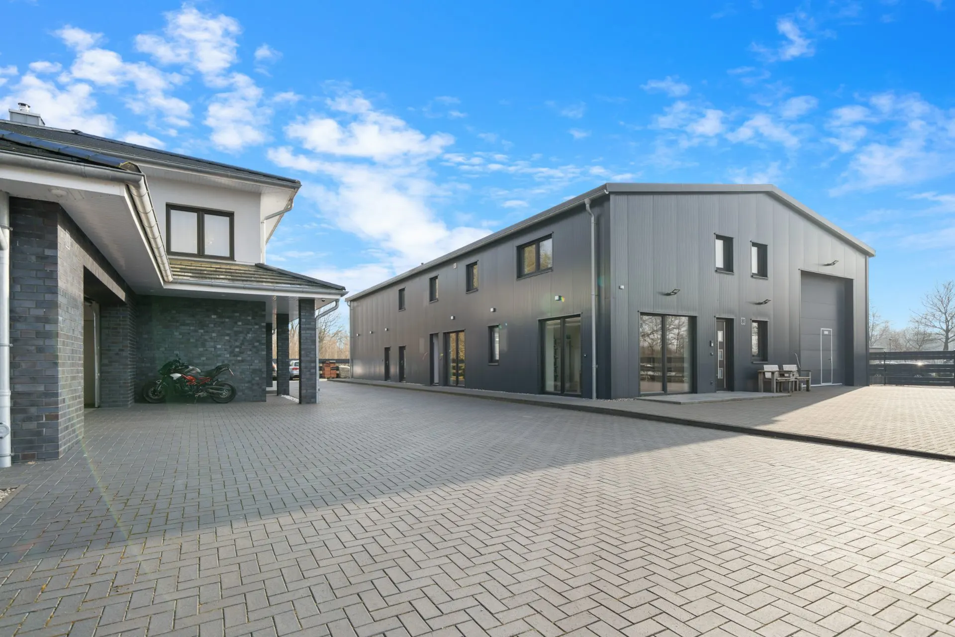 Gepflasterter Hof mit Wohnhaus links und großem modernen Nebengebäude rechts.