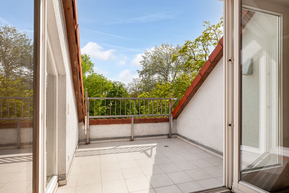 Helle Dachterrasse mit Fliesen, Geländer und Blick auf grüne Bäume.