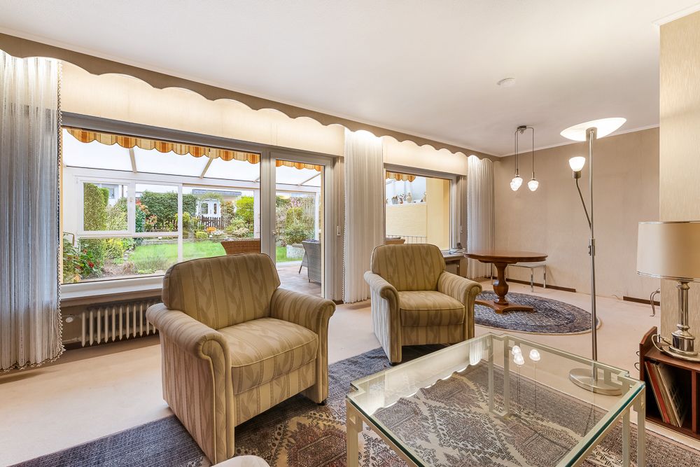 Helles Wohnzimmer mit zwei Sesseln, Glastisch und großem Fenster mit Blick auf den Garten.