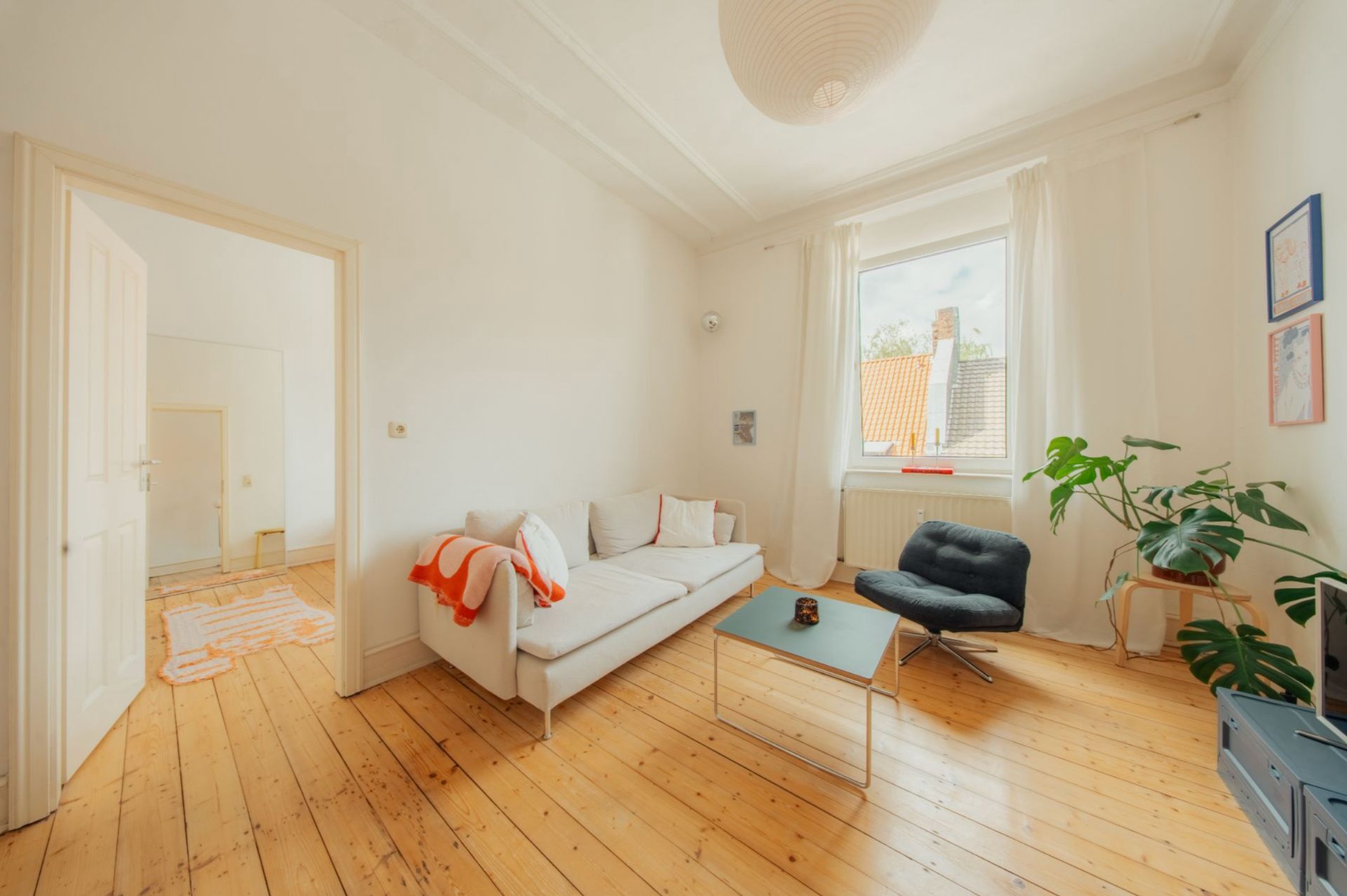Helles Wohnzimmer mit Holzboden, Sofa, Sessel, Couchtisch und großem Fenster mit Blick nach draußen.
