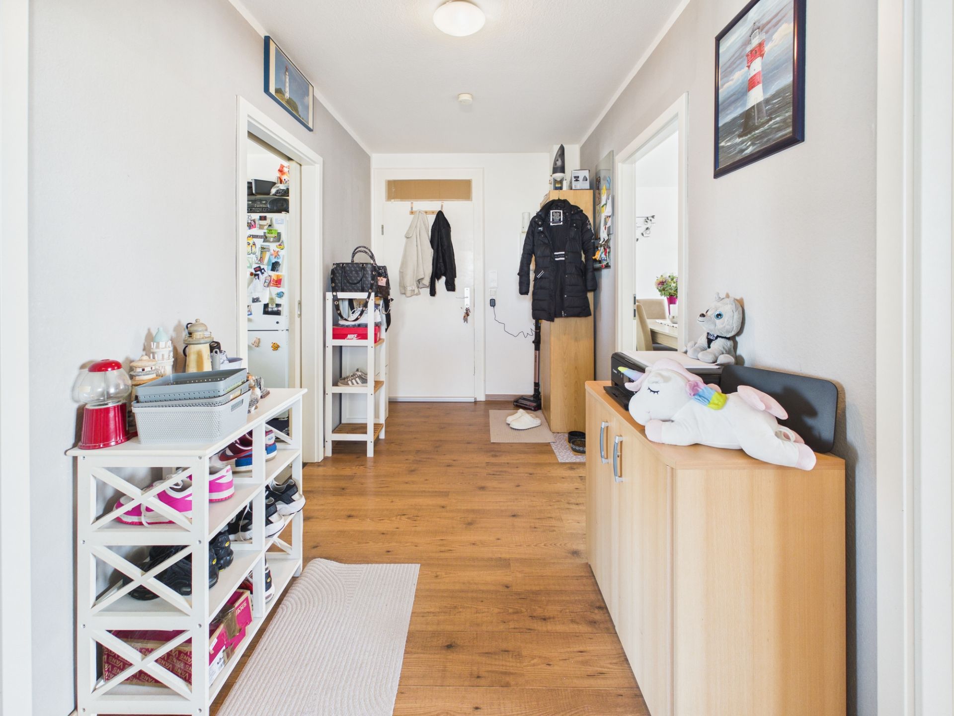 Heller Flur mit Holzfußboden, Schuhregal, Garderobe und Kommode, Jacken und Dekoration sichtbar.