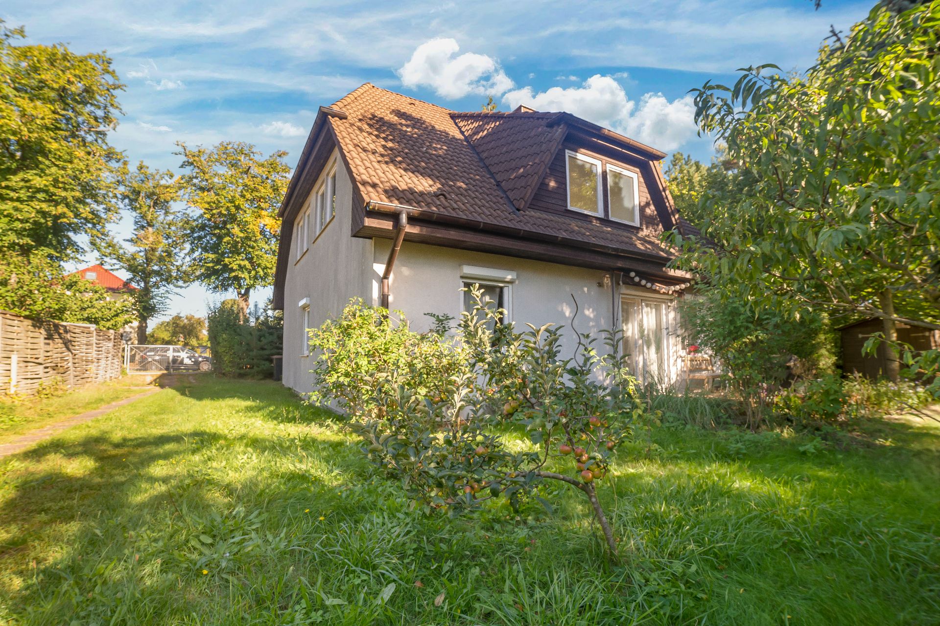 Ein Einfamilienhaus mit Satteldach, Garten und Obstbaum an der Seite bei sonnigem Wetter.