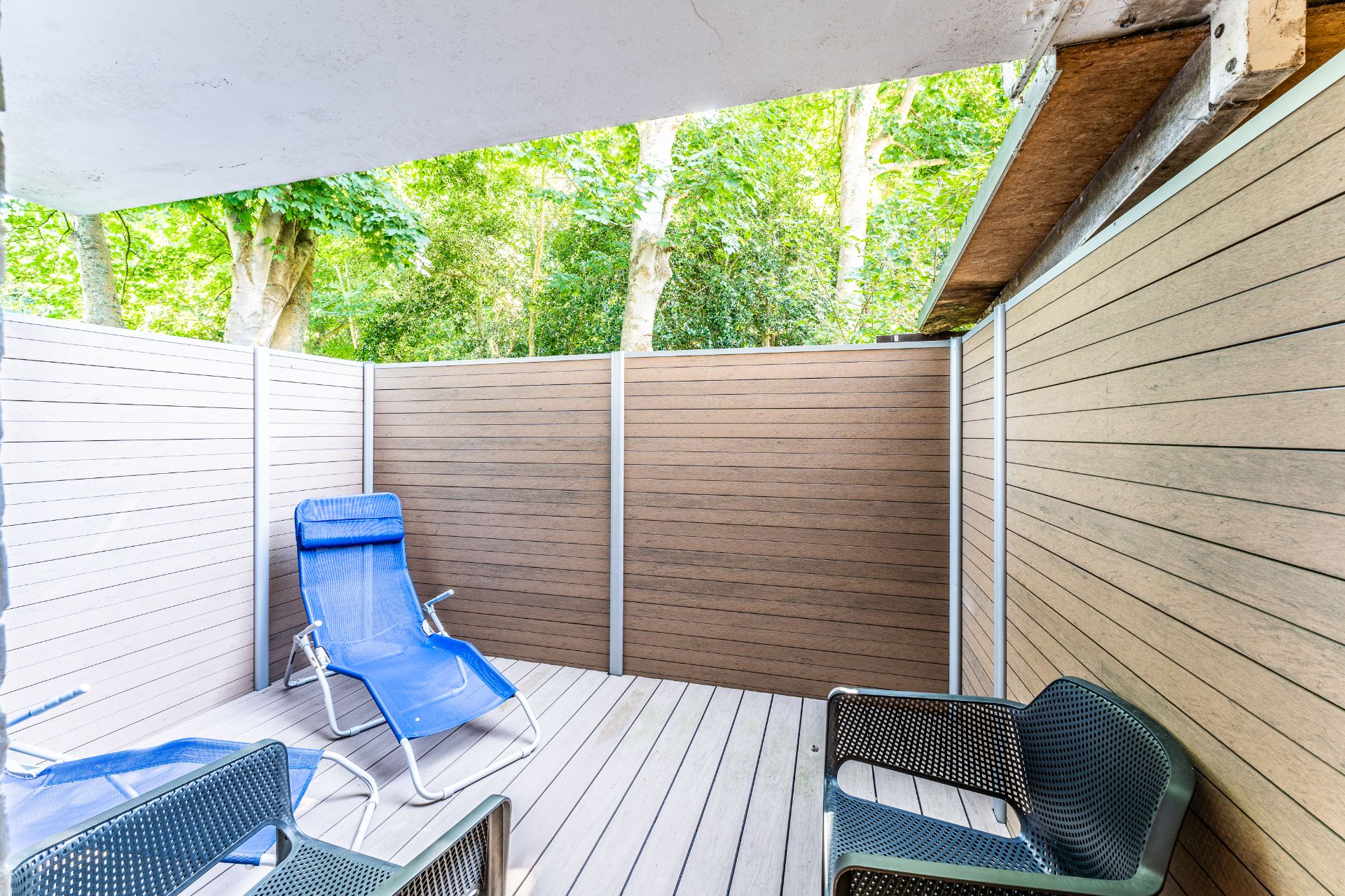 Kleine Terrasse mit Holzverkleidung, zwei blauen Liegestühlen und zwei schwarzen Stühlen.