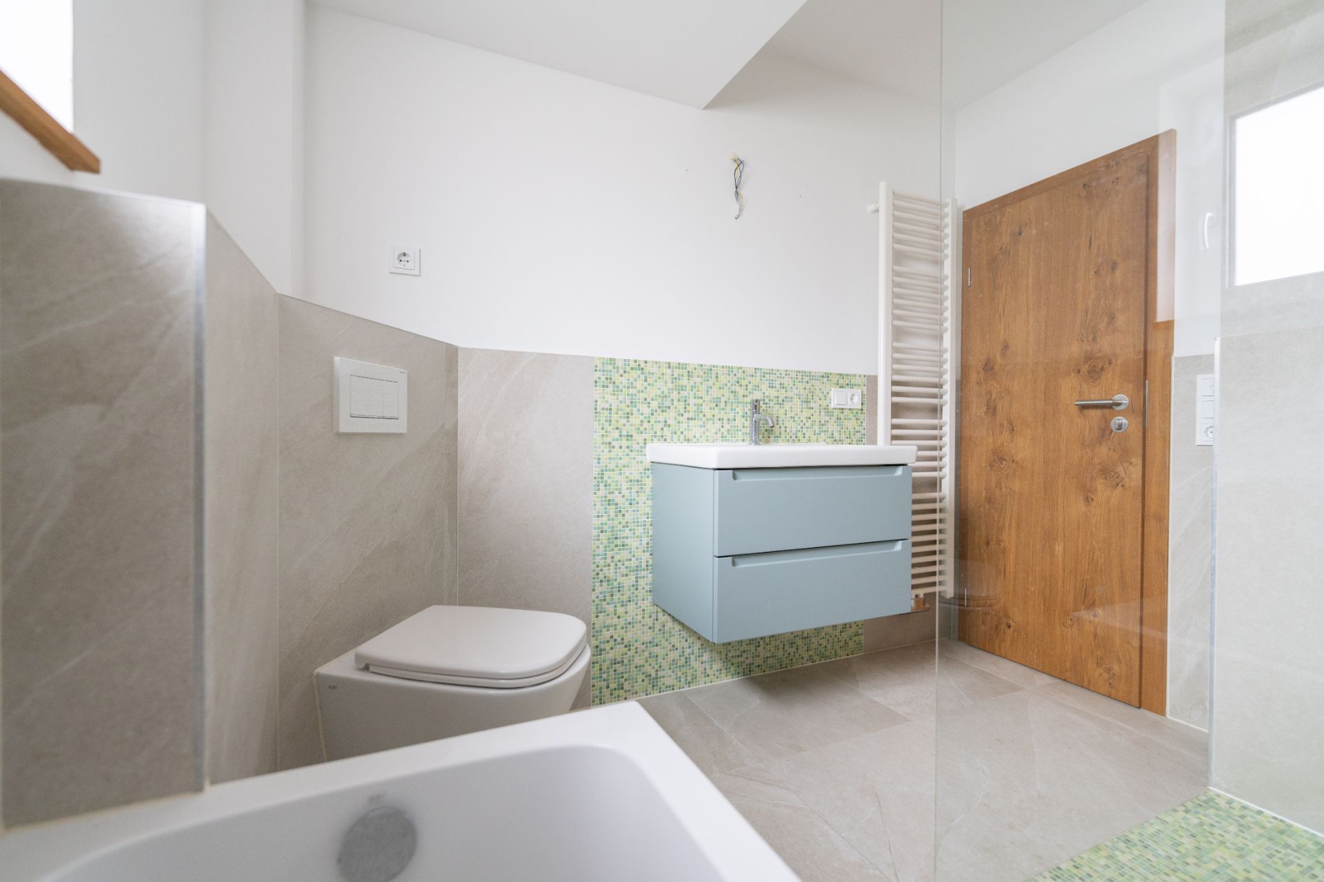 Modernes Badezimmer mit Wandtoilette, Waschbecken, Holz­tür und grün gefliester Wand.