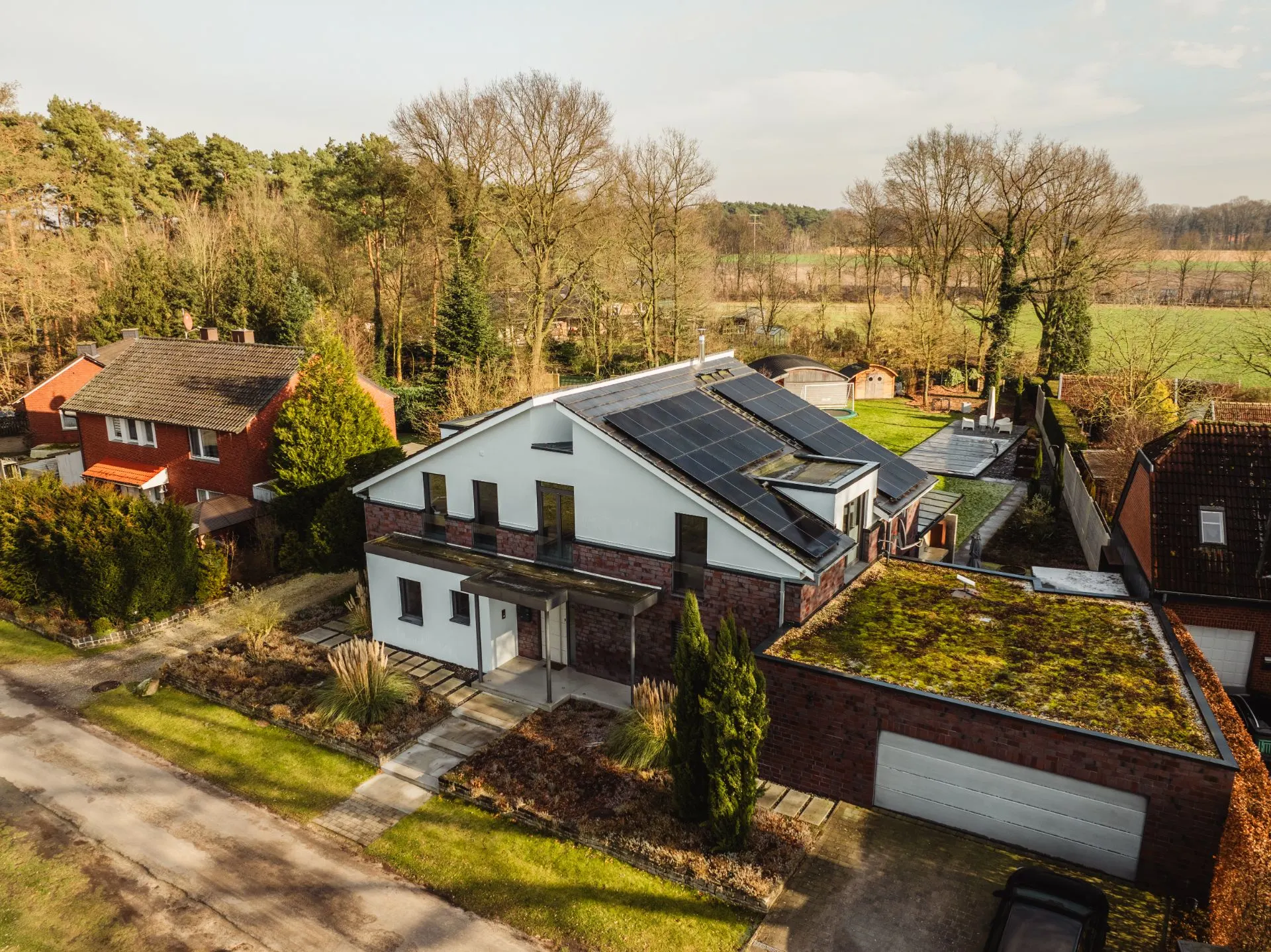 Modernes Wohnhaus mit Solarpanels auf dem Dach und begrüntem Garagendach, umgeben von Bäumen.