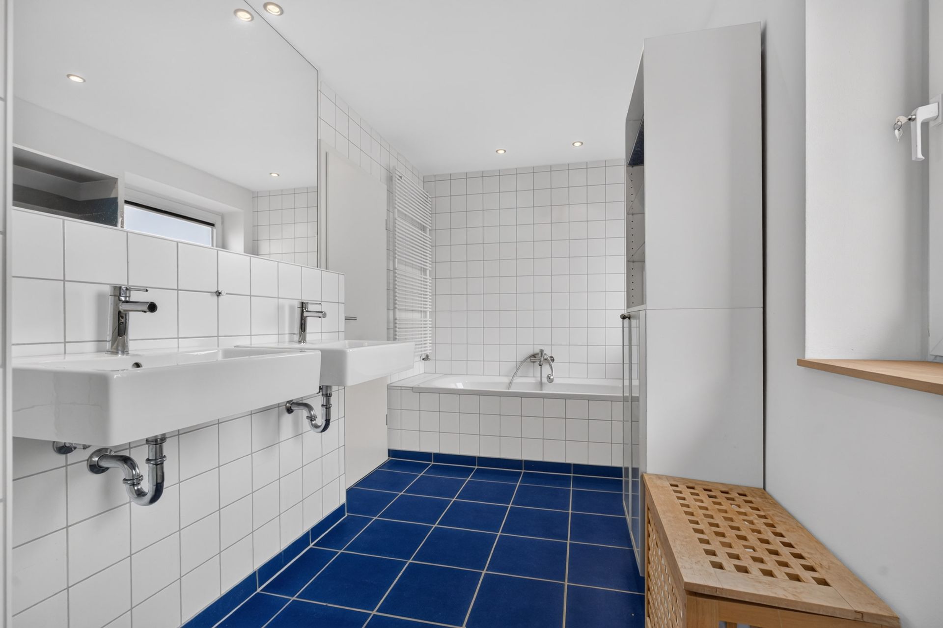 Modernes Badezimmer mit zwei Waschbecken, Badewanne und blau gefliestem Boden.