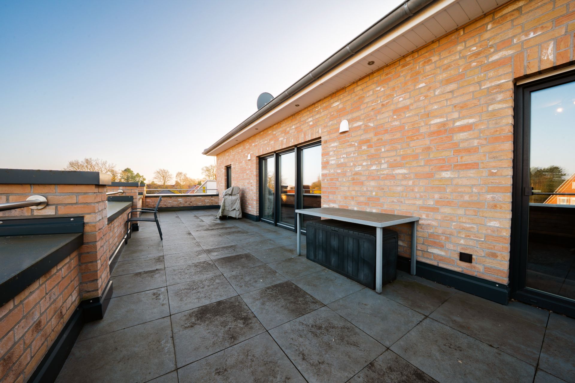 Große, geflieste Dachterrasse mit Tisch und Verkleidung aus rotem Klinkerstein.