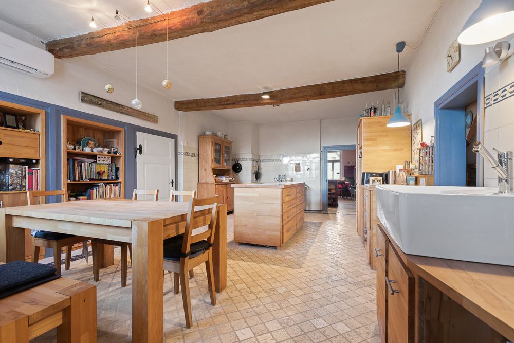 Große Wohnküche mit Holzmöbeln, Esstisch, Kücheninsel und sichtbaren Holzbalken an der Decke.
