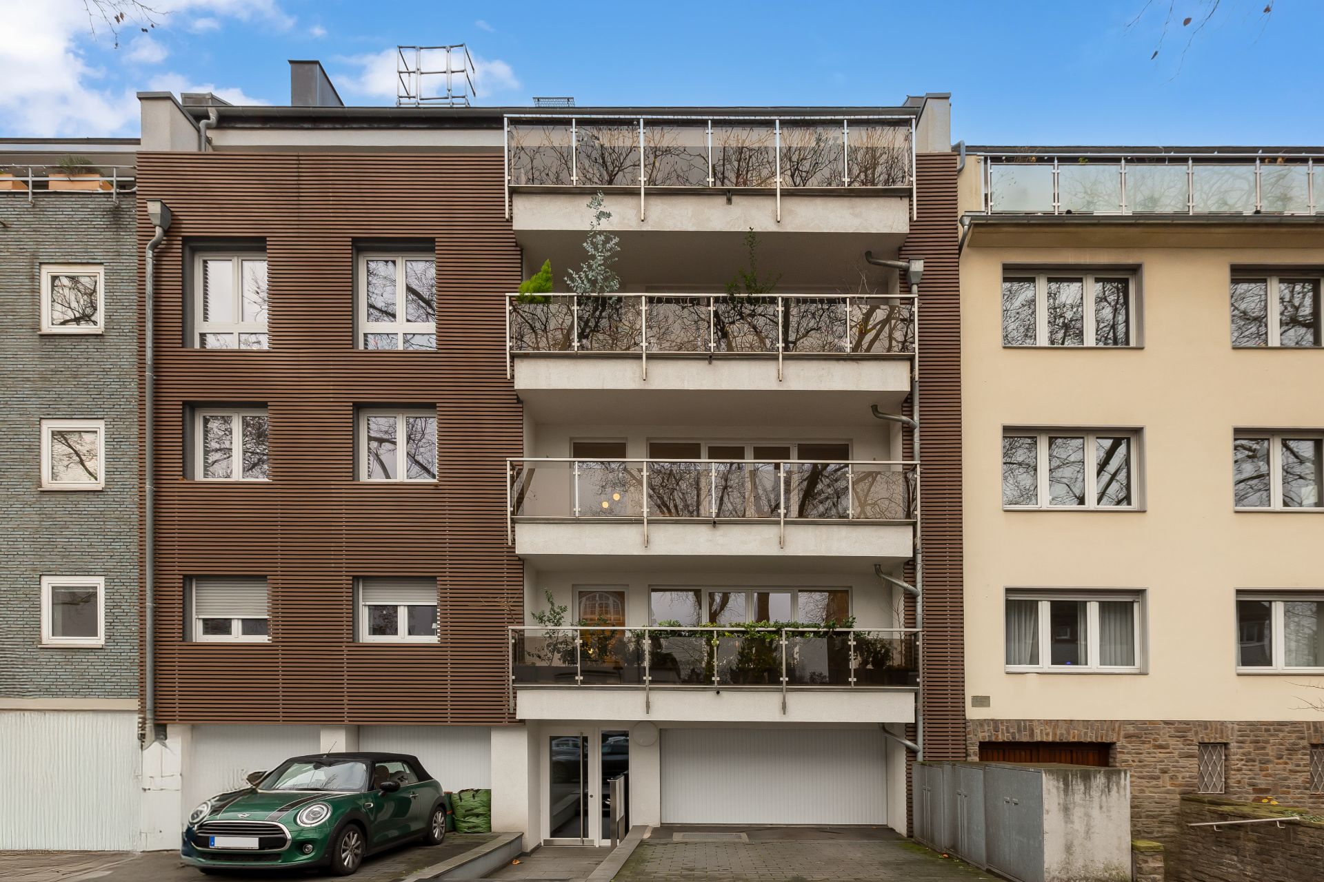 Mehrstöckiges Wohnhaus mit Balkonen, Parkplätzen und einem grünen Auto davor.