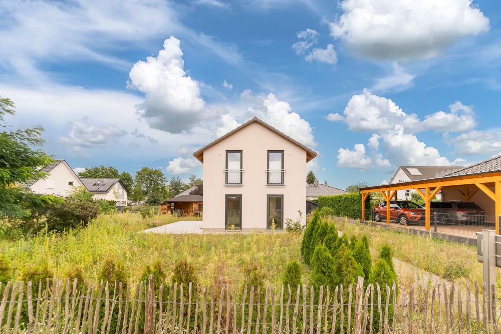 Modernes Einfamilienhaus mit großem Garten, Holzzaun und Carport mit geparkten Autos.