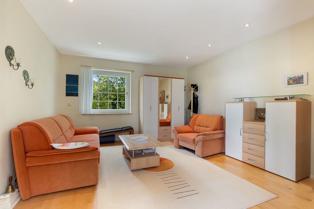 Wohnzimmer mit orangefarbenem Sofa, Sessel, Couchtisch, Schrank, Kommode und großem Fenster.