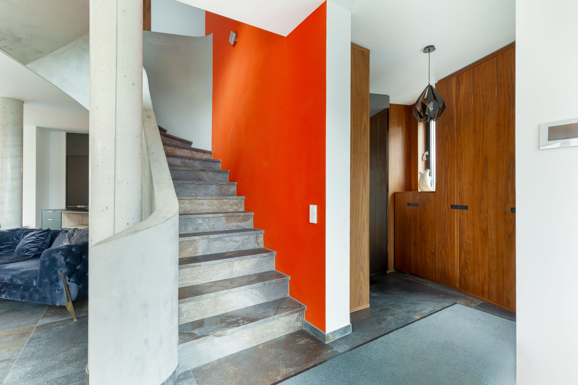 Moderne Treppe mit grauen Stufen und oranger Wand in einem Wohnhausflur.