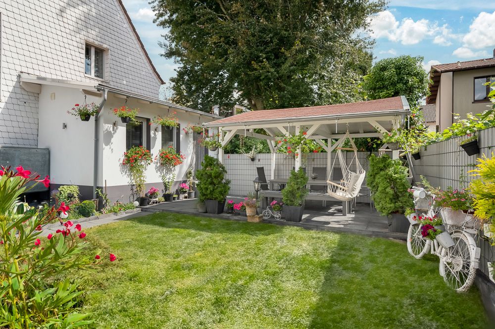 Gepflegter Garten mit Rasenfläche, Sitzbereich unter Pavillon, Blumen und dekorativem Fahrrad.