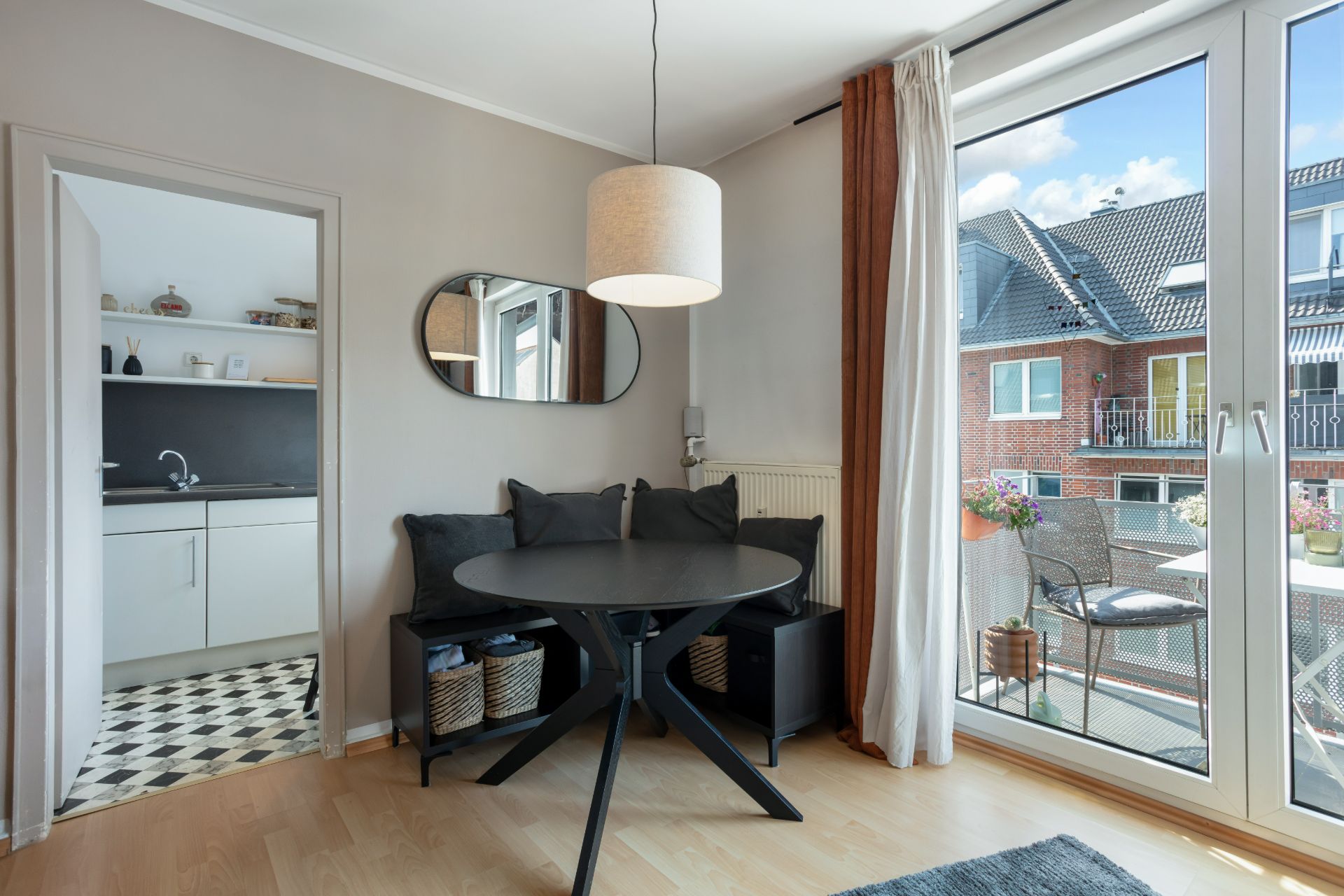 Helles Esszimmer mit rundem Tisch und Zugang zum Balkon, Küche im Hintergrund sichtbar.