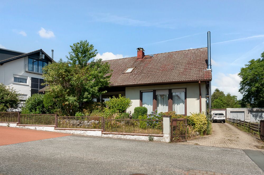 Einfamilienhaus mit Schrägdach, Vorgarten und Einfahrt, umgeben von Bäumen und Sträuchern.