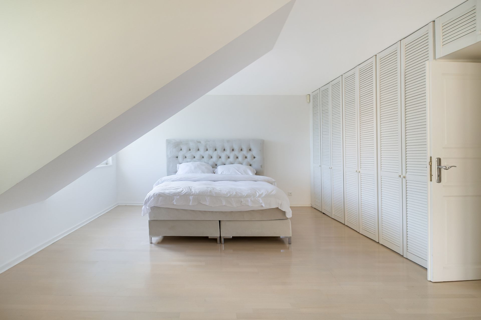 Helles Schlafzimmer mit Doppelbett, Einbauschränken und Dachschräge.