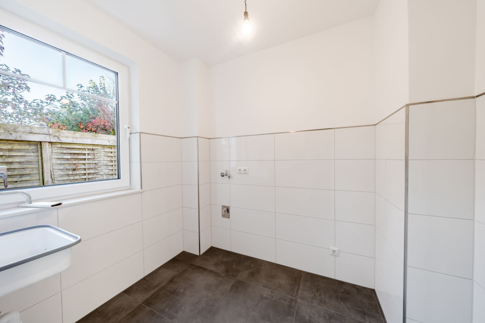 Leerer, gefliester Raum mit Fenster und kleinem Waschbecken an der linken Wand.