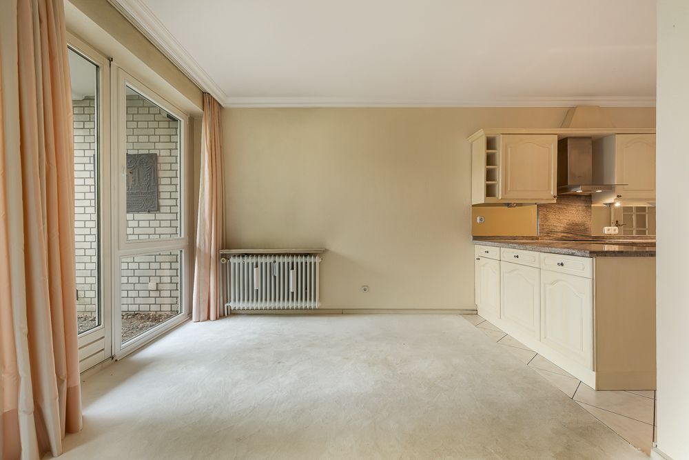 Heller Raum mit offener Küche, großen Fenstern und Heizkörper an der Wand.