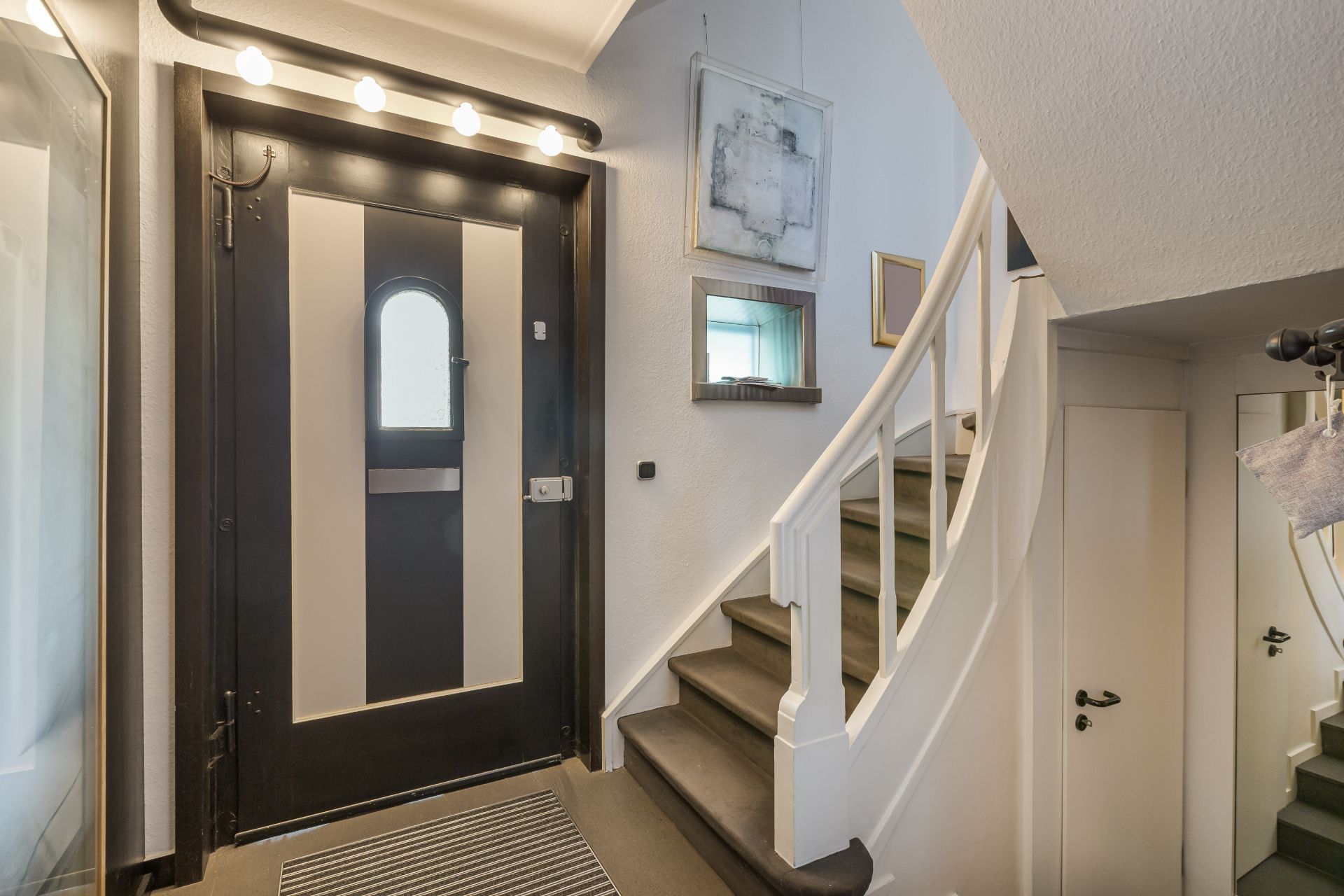 Eingangsbereich mit schwarzer Tür, Treppe nach oben und Wandbildern.