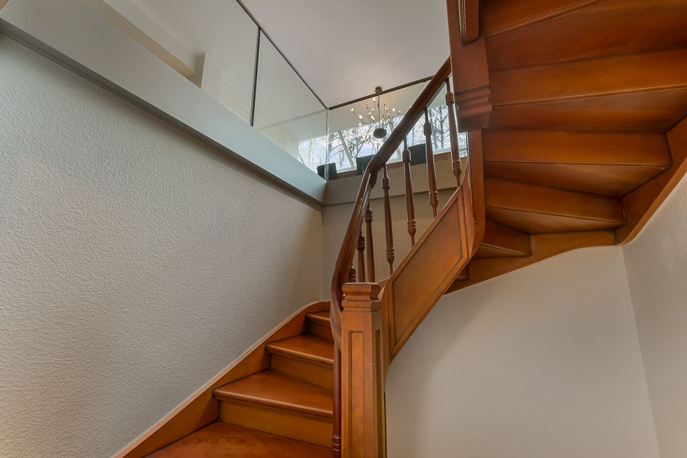 Holztreppe mit Geländer in einem Innenraum, darüber ein Kronleuchter und Fenster.