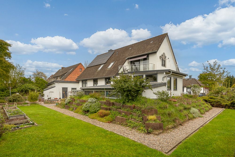 Weißes Einfamilienhaus mit Schrägdach, Garten und Hochbeeten bei sonnigem Wetter.