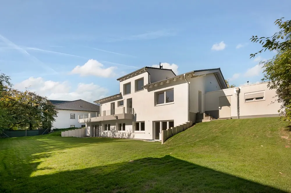 Modernes, mehrstöckiges Wohnhaus mit großem gepflegtem Garten und mehreren Balkonen.