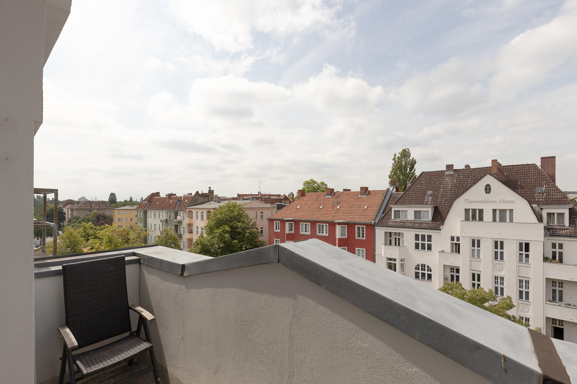Balkon mit Stuhl und Blick auf mehrere Wohnhäuser bei bewölktem Himmel.