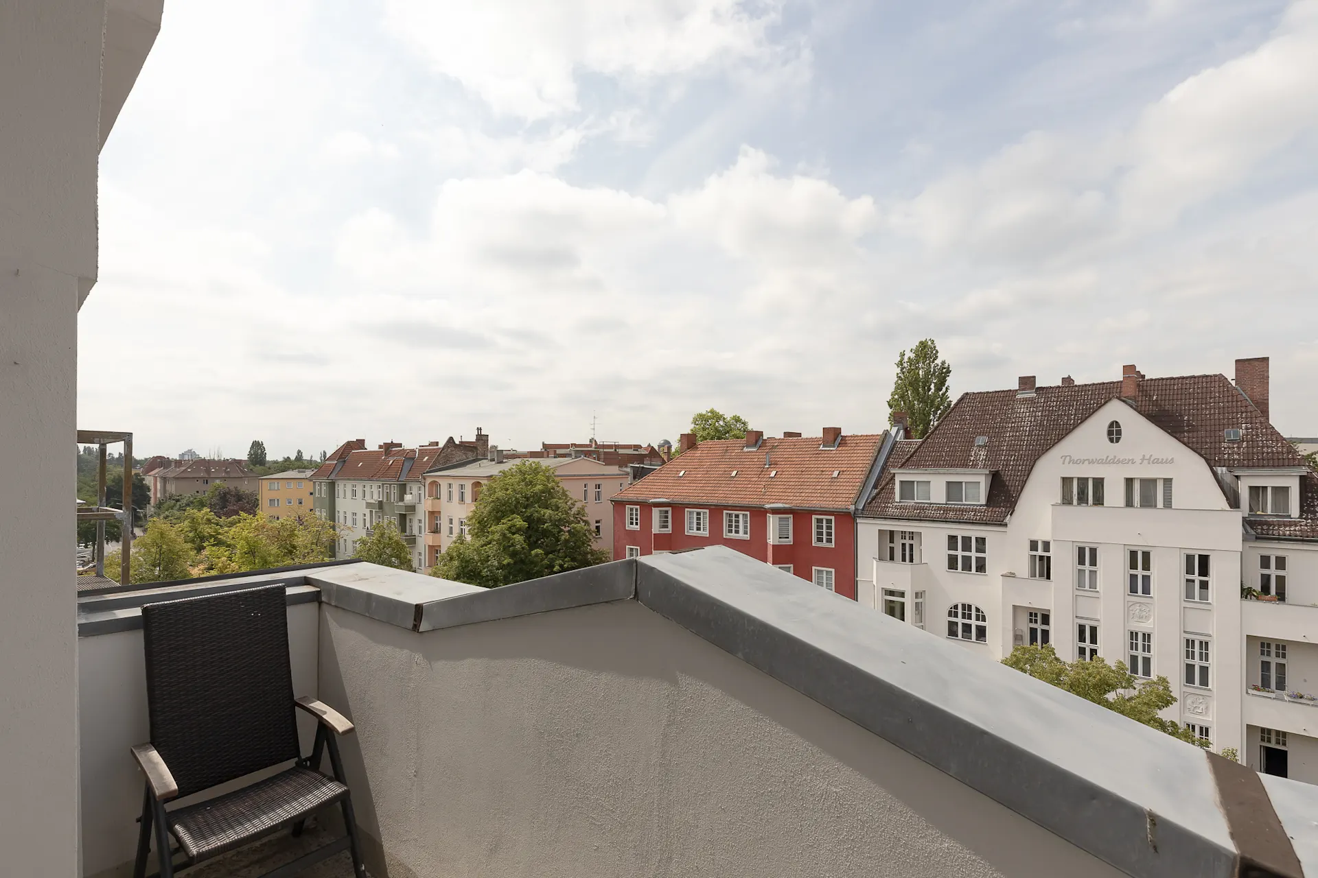 Balkon mit Stuhl und Blick auf mehrere Wohnhäuser bei bewölktem Himmel.
